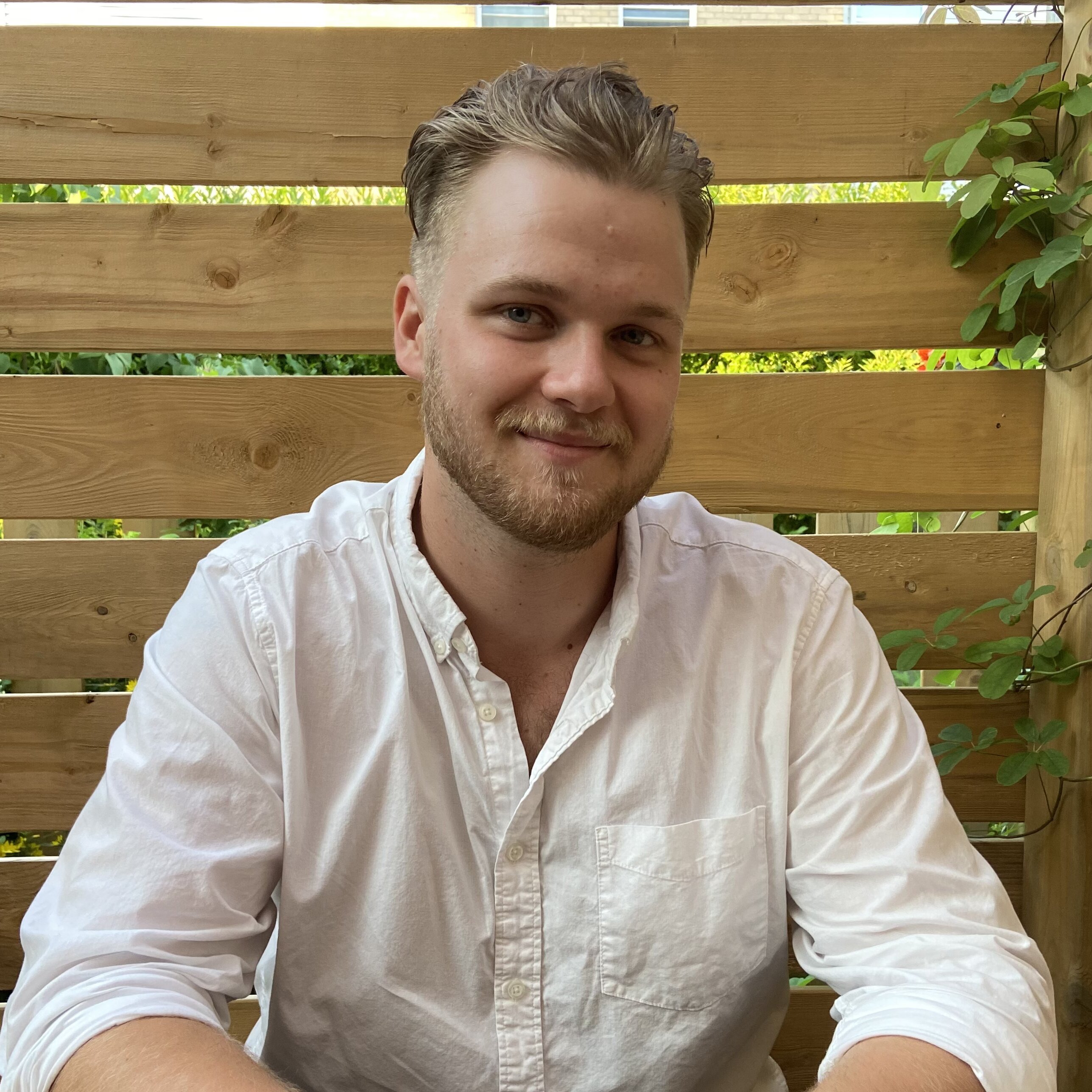 Sam Watts smiling in a white collared shirt on outdoor patio